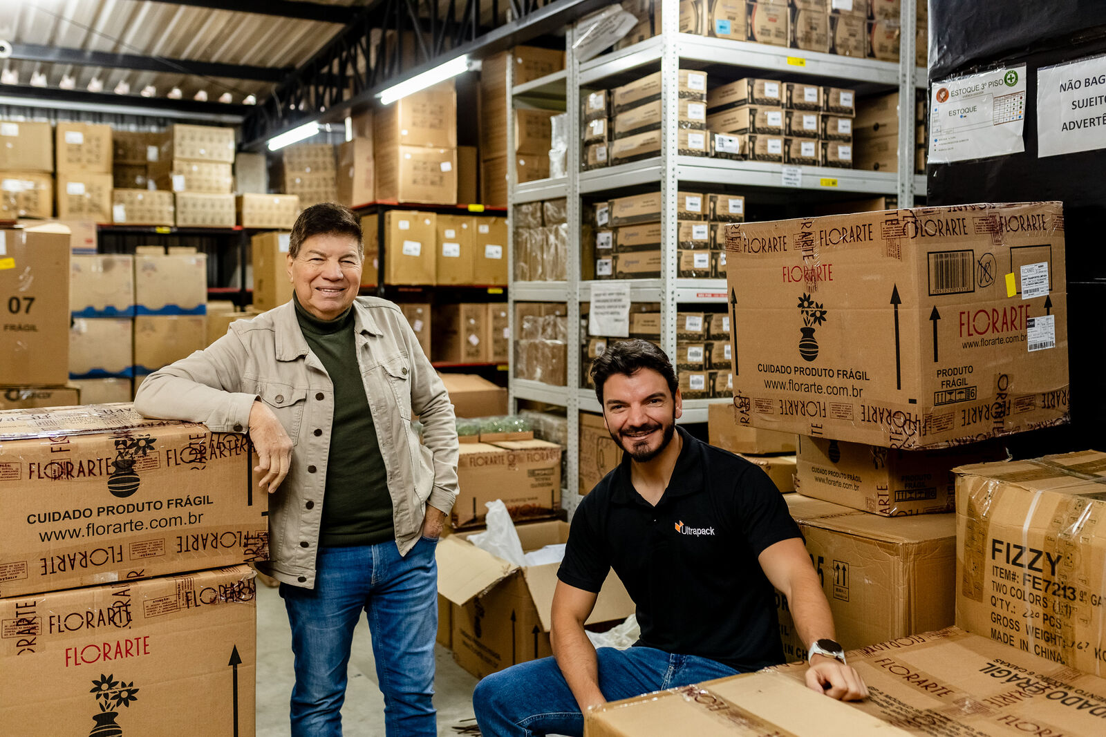 Carlos e seu pai no estoque, entre caixas de mercadorias